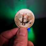 a hand holding a bit coin in front of a green light