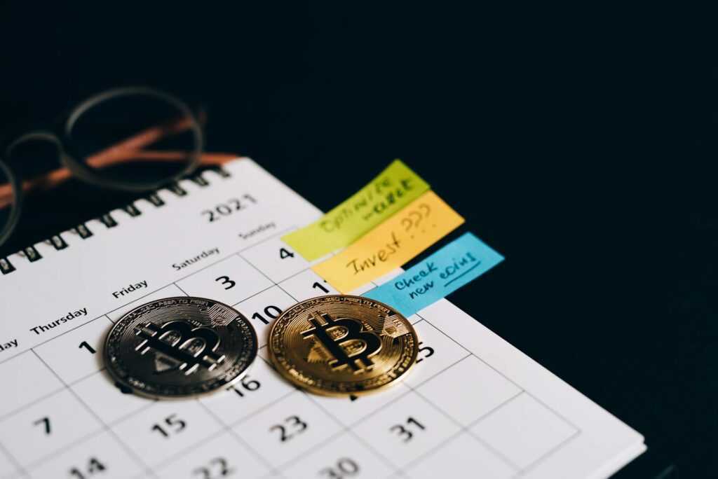 Bitcoin coins placed on a calendar with sticky notes for investment planning.