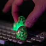 Hand placing glowing crypto coins on a keyboard.